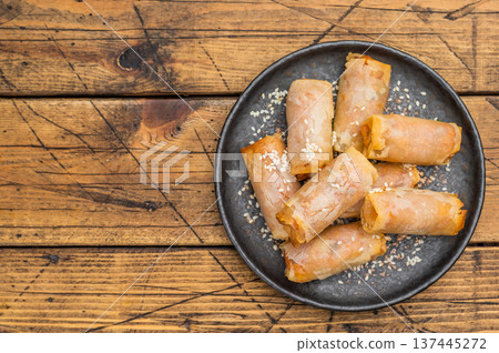 Fried spring rolls snack food on black plate with sesame topping overhead wooden background Fried spring rolls snack food on black plate with sesame topping overhead wooden background 137445272