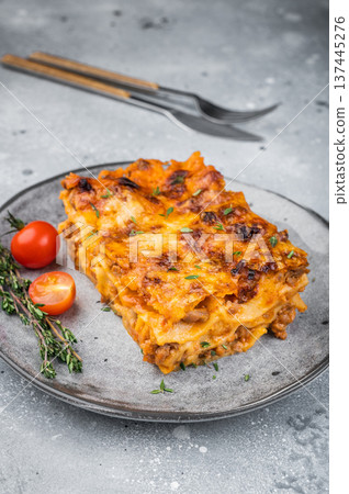 Homemade beef lasagna portion with baked cheese thyme garnish and cherry tomatoes on light stone background 137445276