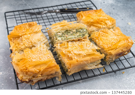 Greek Spanakopita cut into squares on cooling rack, crispy phyllo pastry with spinach and cheese filling, sesame topping, copy space 137445280