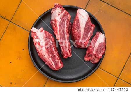 Raw beef short ribs chunks with seasoning and herbs on black plate. Vibrant yellow background with copy space for recipe concepts. 137445300