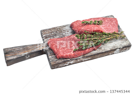 Raw flatiron steaks with thyme on rustic wooden board and carving fork top view on isolated background with copy space 137445344