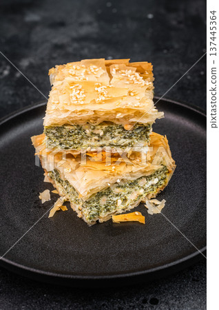 Traditional crispy phyllo pastry with spinach cheese filling cut into pieces, modern rustic presentation Traditional crispy phyllo pastry with spinach cheese filling cut into pieces, modern rustic presentation 137445364