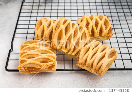Homemade apple pastries with flaky puff dough and fruit filling on metal rack. Minimal flatlay dessert baking concept Homemade apple pastries with flaky puff dough and fruit filling on metal rack. Minimal flatlay dessert baking concept 137445368