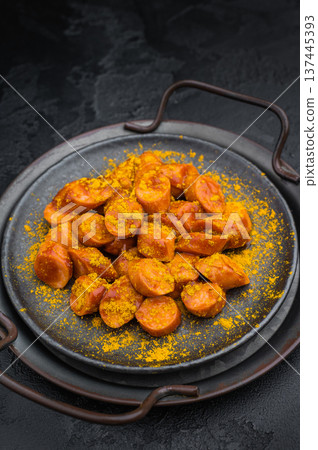 German currywurst, sausages with curry spice served on rustic metal plate over dark textured background perfect for street food and stock imagery. 137445393
