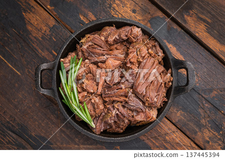 Savory wild venison ragout slowcooked and tender with rosemary aromatics presented in castiron pan over textured rustic wooden surface 137445394