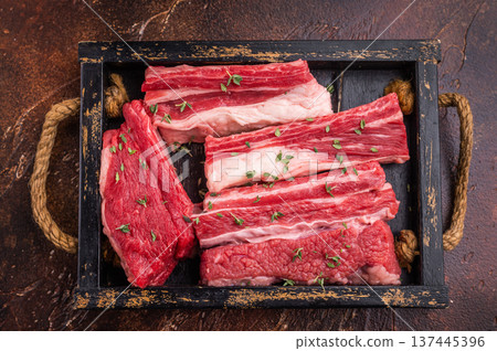 Raw beef short ribs with thyme and fork on a rustic dark background. Excellent for menu design or a butcher shop advertisement. Raw beef short ribs with thyme and fork on a rustic dark background. Excellent for menu design or a butcher shop advertisement. 137445396