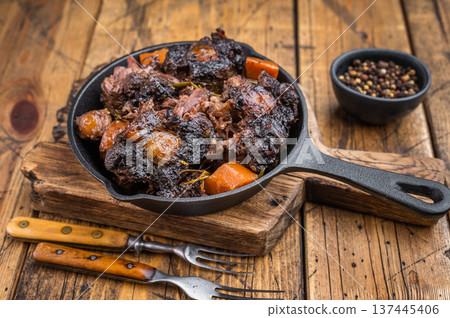 Braised beef oxtail stew with carrots and rosemary in cast iron skillet on rustic wooden table, rich dark sauce Braised beef oxtail stew with carrots and rosemary in cast iron skillet on rustic wooden table, rich dark sauce 137445406