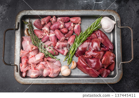 Raw duck liver, hearts, and gizzards on metal tray with garlic and rosemary on dark textured background, fresh poultry offal. Raw duck liver, hearts, and gizzards on metal tray with garlic and rosemary on dark textured background, fresh poultry offal. 137445411