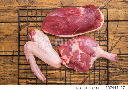 Fresh uncooked duck cuts breast fillet thigh and wingarranged on cooling grid against scratched wood surface perfect for culinary preparation visuals. Fresh uncooked duck cuts breast fillet thigh and wingarranged on cooling grid against scratched wood surface perfect for culinary preparation visuals. 137445417