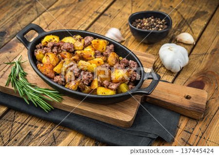 Rustic beef hash with golden fried potatoes served in a cast iron pan on a wooden table, seasoned with garlic, pepper and rosemary. Rustic beef hash with golden fried potatoes served in a cast iron pan on a wooden table, seasoned with garlic, pepper and rosemary. 137445424