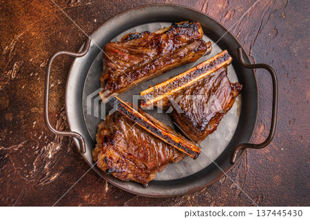 Barbecue Meat Dish: Succulent BBQ short ribs styled with herbs on an aged tray. High contrast, premium dark photography. 137445430