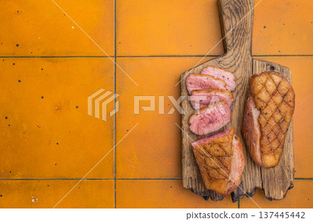 Roasted duck fillet with crispy skin served on aged board against warm orange tiles ideal for recipe content and gourmet food photography. 137445442