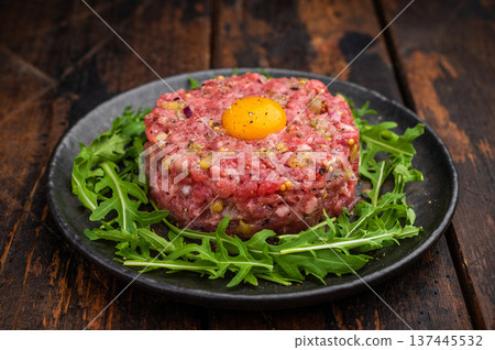 Raw beef tartare with egg yolk and arugula on wooden surface great for gourmet cooking protein rich meals and high quality food photography. 137445532