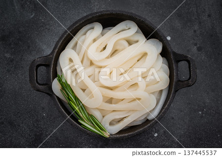 Raw calamari squid loops on black textured surface with herbs offering minimal ocean seafood ingredient concept for culinary design Raw calamari squid loops on black textured surface with herbs offering minimal ocean seafood ingredient concept for culinary design 137445537