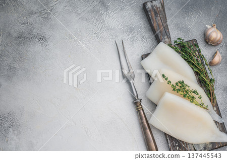 Raw calamari arranged with herbs on weathered wood against a gray stone backdrop ideal for culinary seafood stock concepts. 137445543
