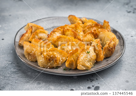 Crispy pan fried jiaozi dumplings with sesame served on dark plate. Asian mandu potstickers Crispy pan fried jiaozi dumplings with sesame served on dark plate. Asian mandu potstickers 137445546