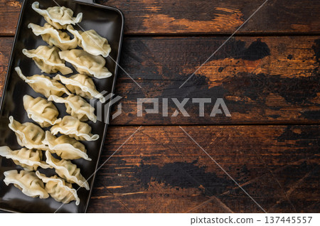 Traditional gyoza, jiaozi or mandu served as an authentic oriental appetizer. Steamed Asian dumplings arranged on a dark rectangular plate with chopsticks on a rustic wooden table. 137445557