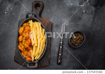 German currywurst with fries in a cast iron pan on dark background perfect for street food visuals fast food ads and stock images. German currywurst with fries in a cast iron pan on dark background perfect for street food visuals fast food ads and stock images. 137445566
