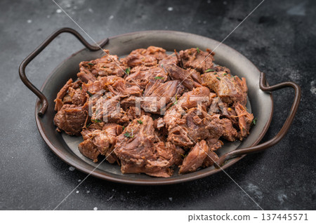 Rustic braised moose venison stew, shredded and savory, plated with fresh rosemary on a metal dish over dark stone background 137445571