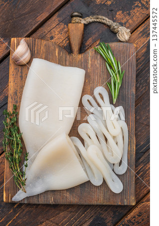 White fresh calamari ring displayed on rustic board with herbs ideal for seafood recipes menus and professional food photography. White fresh calamari ring displayed on rustic board with herbs ideal for seafood recipes menus and professional food photography. 137445572