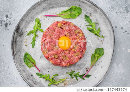 Raw beef tartare with yolk and greens on stone dish over gray backdrop great for protein rich meals gourmet cooking and high quality food photography. Raw beef tartare with yolk and greens on stone dish over gray backdrop great for protein rich meals gourmet cooking and high quality food photography. 137445574