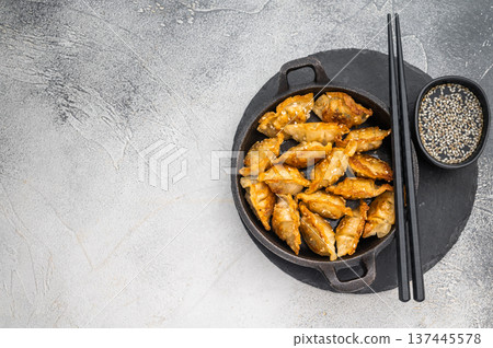 Golden fried dumplings jiaozi sprinkled with sesame served in black skillet on bright stone surface perfect Asian snack. 137445578