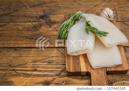 Raw calamari and fresh rosemary on vintage wood board captured for culinary design seafood menus and Mediterranean style visuals 137445585