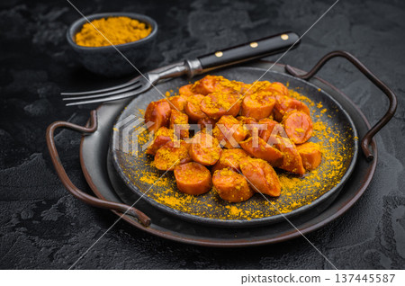 German currywurst, sausages with curry spice served on rustic metal plate over dark textured background perfect for street food and stock imagery. German currywurst, sausages with curry spice served on rustic metal plate over dark textured background perfect for street food and stock imagery. 137445587