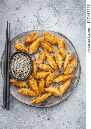 Golden fried dumplings gyoza with sesame seeds on gray tableware. Crunchy Asian potstickers shot top view on gray surface. Golden fried dumplings gyoza with sesame seeds on gray tableware. Crunchy Asian potstickers shot top view on gray surface. 137445588