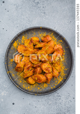 Traditional currywurst sprinkled with curry spice on textured surface great for German street food concepts and culinary stock content. Traditional currywurst sprinkled with curry spice on textured surface great for German street food concepts and culinary stock content. 137445593