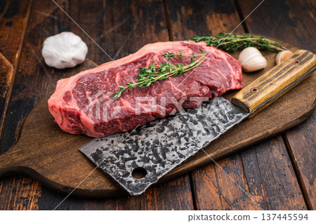 Dry aged striploin beef steak with thyme sprigs and rustic meat cleaver on dark wood surface ideal for culinary blogs and grill promotions. Dry aged striploin beef steak with thyme sprigs and rustic meat cleaver on dark wood surface ideal for culinary blogs and grill promotions. 137445594