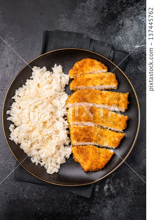 Delicious katsu style dish, featuring a perfectly cooked chicken meat cutlet served alongside steamed rice for a balanced meal. black background. top view Delicious katsu style dish, featuring a perfectly cooked chicken meat cutlet served alongside steamed rice for a balanced meal. black background. top view 137445762