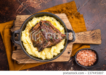 Close-up of tender beef short ribs, beautifully caramelized and resting on a bed of creamy mashed potatoes, creating an inviting culinary scene. brown background. top view 137445807