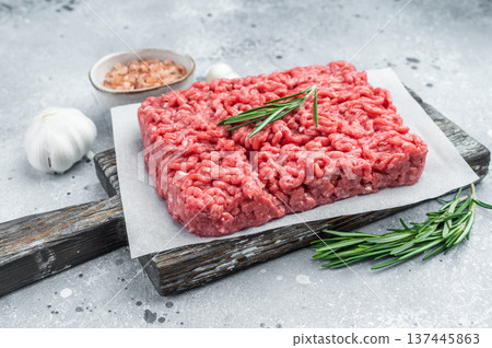 Fresh raw ground mince beef meat with rosemary on parchment over rustic wooden board and concrete background ideal for cooking and protein visuals. Fresh raw ground mince beef meat with rosemary on parchment over rustic wooden board and concrete background ideal for cooking and protein visuals. 137445863