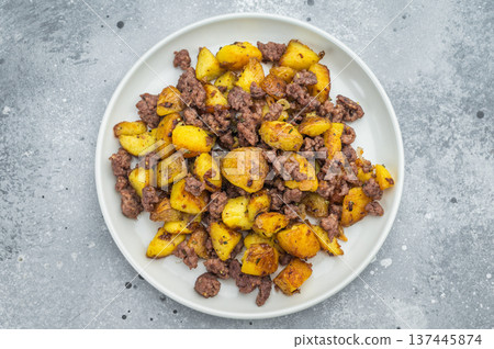 Crispy fried potatoes with ground beef served on a white plate, hearty homemade hash on a rustic grey background.. 137445874