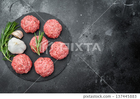 Fresh raw meatballs or Polpette with rosemary and pepper on round black slate board over dark background ideal for cooking and protein-rich themes. Fresh raw meatballs or Polpette with rosemary and pepper on round black slate board over dark background ideal for cooking and protein-rich themes. 137445883