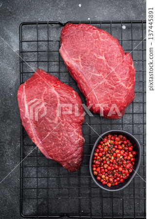Marbled Wagyu beef chuck steaks similar to angus and yakiniku cuts placed on grill rack with pepper bowl on dark stone backdrop great for butcher photography. Marbled Wagyu beef chuck steaks similar to angus and yakiniku cuts placed on grill rack with pepper bowl on dark stone backdrop great for butcher photography. 137445891