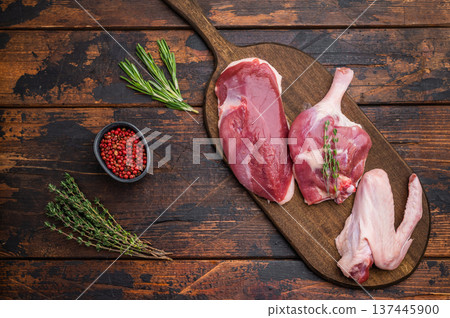 Plucked raw duck meat selection displayed on rustic board with seasoning against dark wood backdrop showcasing premium poultry. 137445900