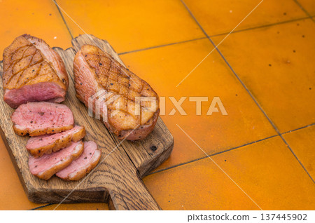 Tender seared duck breast sliced on wooden cutting board with bright tile backdrop great for cooking articles and stock marketplaces. 137445902