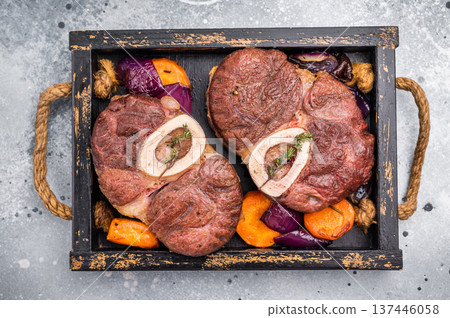 Flavorful ossobuco garnished with fresh herbs, osso buco shank ideal for impressing guests at your next dinner party. grey background. top view Flavorful ossobuco garnished with fresh herbs, osso buco shank ideal for impressing guests at your next dinner party. grey background. top view 137446058