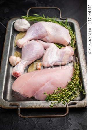 Raw chicken assortment: breast, leg, drumstick, and wing with fresh herbs and garlic on a metal tray, on a dark textured background. Copy space. Raw chicken assortment: breast, leg, drumstick, and wing with fresh herbs and garlic on a metal tray, on a dark textured background. Copy space. 137446135