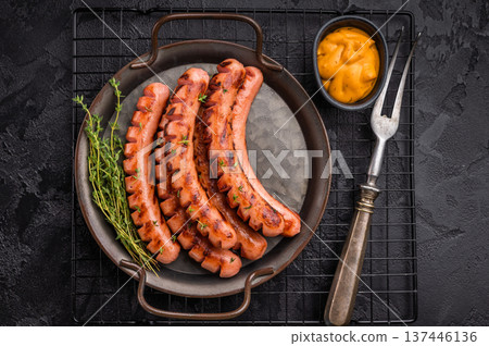 Grilled and cut sausages (frankfurters/wieners) on a rustic platter with mustard sauce and thyme on a dark textured background. Grilled and cut sausages (frankfurters/wieners) on a rustic platter with mustard sauce and thyme on a dark textured background. 137446136
