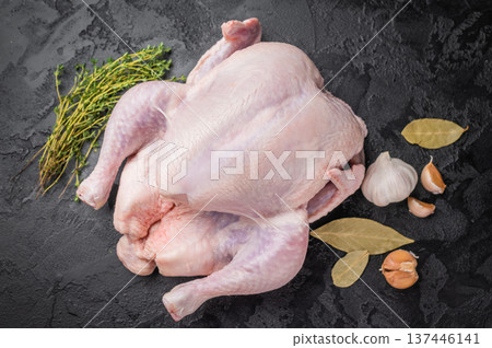 Raw whole chicken with fresh thyme and garlic cloves on a dark, black textured stone background. Preparing to cook poultry. 137446141