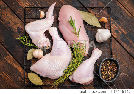 Raw chicken cuts (breast, leg, wing) on a rack with thyme, rosemary, garlic, and peppercorns on dark rustic wood. Ready for seasoning. Raw chicken cuts (breast, leg, wing) on a rack with thyme, rosemary, garlic, and peppercorns on dark rustic wood. Ready for seasoning. 137446142