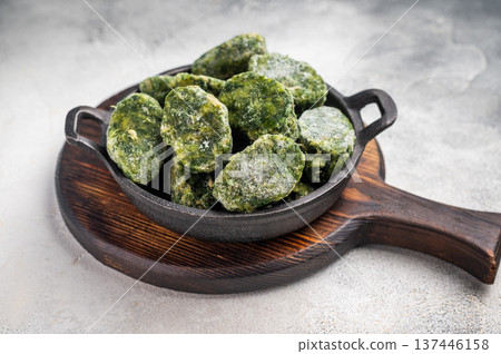 Overhead shot of frozen spinach blocks in a cast iron skillet on a wooden board. Grey textured background with copy space. Overhead shot of frozen spinach blocks in a cast iron skillet on a wooden board. Grey textured background with copy space. 137446158