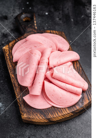 Overhead view of cold cuts (mortadella) on a small wooden board. Gourmet deli concept on a dramatic, black texture background. Overhead view of cold cuts (mortadella) on a small wooden board. Gourmet deli concept on a dramatic, black texture background. 137446163