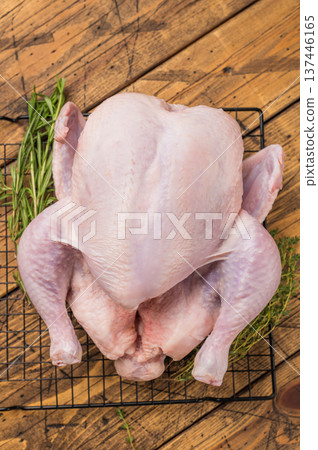 Whole fresh raw chicken on a cooling rack with rosemary and thyme. Ready for cooking on a rustic wooden table. 137446165