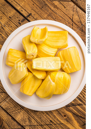 Sweet, golden yellow jackfruit pods (bulbs) served on a white plate on a rustic wooden table. Fresh, tropical fruit snack. 137446167