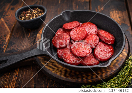 Fried Turkish sucuk (sujuk) slices in a cast iron pan with thyme and spices on a dark rustic wooden table. Fried Turkish sucuk (sujuk) slices in a cast iron pan with thyme and spices on a dark rustic wooden table. 137446182