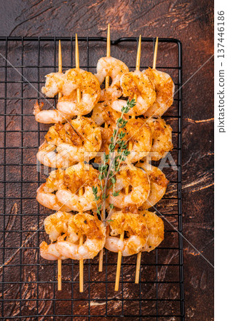 Appetizing BBQ shrimp prawn kebab seasoned with herbs and spices. Ready-to-eat grilled seafood on a wooden stick against a dark backdrop. Appetizing BBQ shrimp prawn kebab seasoned with herbs and spices. Ready-to-eat grilled seafood on a wooden stick against a dark backdrop. 137446186